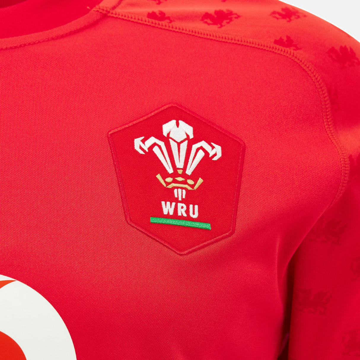 Close-up of the Wales WRU 26/27 Replica Home Jersey by Macron, highlighting the Welsh Rugby Union (WRU) logo with three white feathers above the initials “WRU,” and showcasing the detail and quality of this official replica shirt from Macron.
