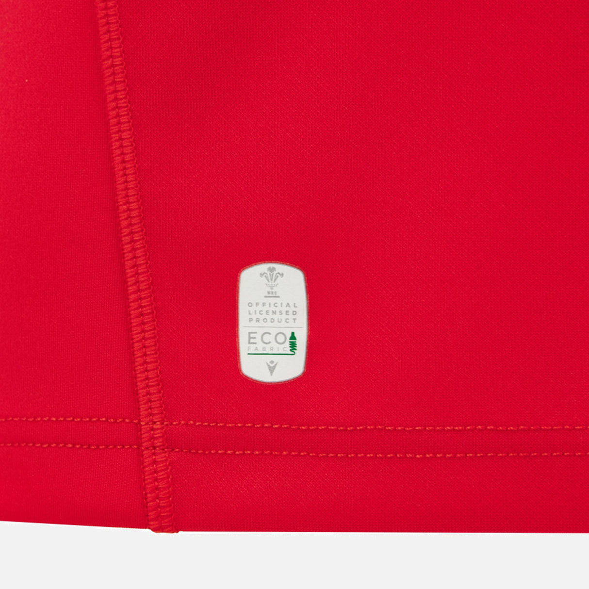 Close-up of the red fabric from the Wales WRU 26/27 Replica Home Jersey by Macron, highlighting a white label that reads “Official Product ECO” with a small tree graphic—signifying the use of eco-friendly materials in this Macron rugby shirt.