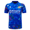 The Italy 26/27 Home Replica Jersey by Macron features a blue short-sleeve design with an abstract geometric pattern, the Italian flag badge, sponsor logo “Vittoria Assicurazioni,” and a white Macron brand logo. Inspired by classic Italy Rugby Jersey styles, this jersey embodies both sporty appeal and national pride.