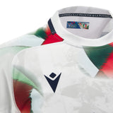 Close-up of the Italy 26/27 Away Replica Jersey by Macron, featuring abstract green and red patterns on a crisp white base, a navy Macron logo, and a collar lined with Italian flag details and inner text.