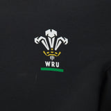 The Wales WRU 26/27 Goalpost Fan Cotton T-Shirt by Macron features black fabric adorned with the Welsh Rugby Union (WRU) logo in white, gold, and green—including three stylized feathers above the “WRU” lettering—making it a perfect choice for fans wanting a classic Welsh Rugby look.