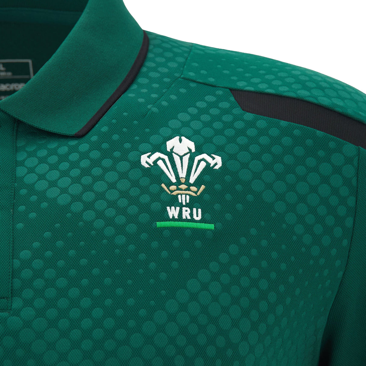 Close-up of the Wales WRU 26/27 Travel Poly Polo by Macron, a green polo shirt with a honeycomb pattern, featuring the WRU logo and lettering embroidered in white and gold on the chest.