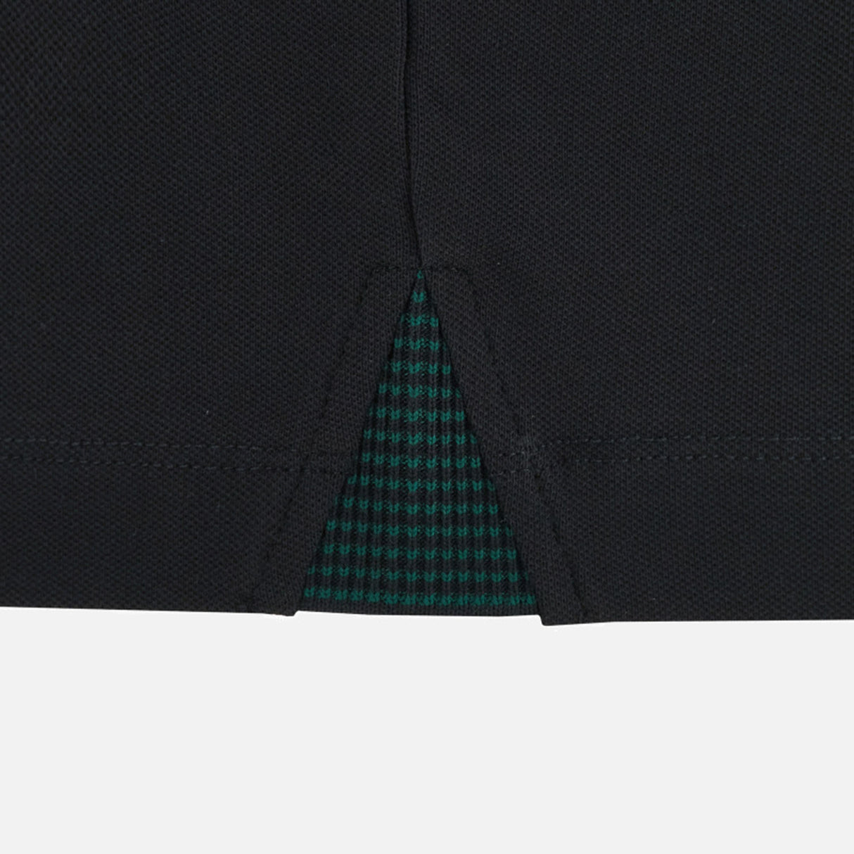 Close-up of a black fabric garment hem with a center slit, revealing a green and black checkered inner lining underneath—showcasing refined detailing reminiscent of the finishes seen on the Wales WRU 26/27 Travel Cotton Polo by Macron.