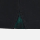 Close-up of a black fabric garment hem with a center slit, revealing a green and black checkered inner lining underneath—showcasing refined detailing reminiscent of the finishes seen on the Wales WRU 26/27 Travel Cotton Polo by Macron.