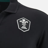 The Wales WRU 26/27 Travel Cotton Polo by Macron is a black polo shirt styled like a classic Macron rugby top, featuring a white WRU logo with three feathers inside a shield on the left chest.