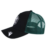 The Wales WRU 26/27 Trucker Cap by Macron features black and green mesh panels, a white emblem on the front, and a logo on the brim. Shown in left side profile, this stylish cap is crafted with quality by Macron—perfect for Wales Rugby supporters.