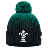 The Wales WRU 26/27 Pom-Pom Beanie by Macron features a green and black knit design with a pom-pom, showcasing the WRU logo in white on the front fold and an additional white logo on the side. This classic beanie by Macron is perfect for any Wales Rugby fan wanting to stay warm in style.