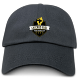 The EMB S&S Activewear Chicago Riot Adult Low-Profile Cotton Twill Dad Cap is black with embroidered "Chicago Riot Rugby Football Club" logo, a raised fist, and gold accents on the front.
