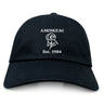 The Amoskeag Rugby Club Adult Low-Profile Cotton Twill Dad Cap by EMB S&S Activewear features “AMOSKEAG” and “Est. 1984” embroidered in white above a ram’s head logo on black cotton twill.