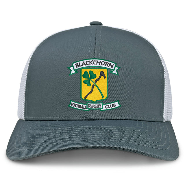 The Blackthorn RFC Retro Trucker Cap by EMB S&S Activewear features a gray and white mesh back, embroidered crest logo with shamrock and blackthorn stick on a yellow shield, and a snapback closure for adjustable fit.