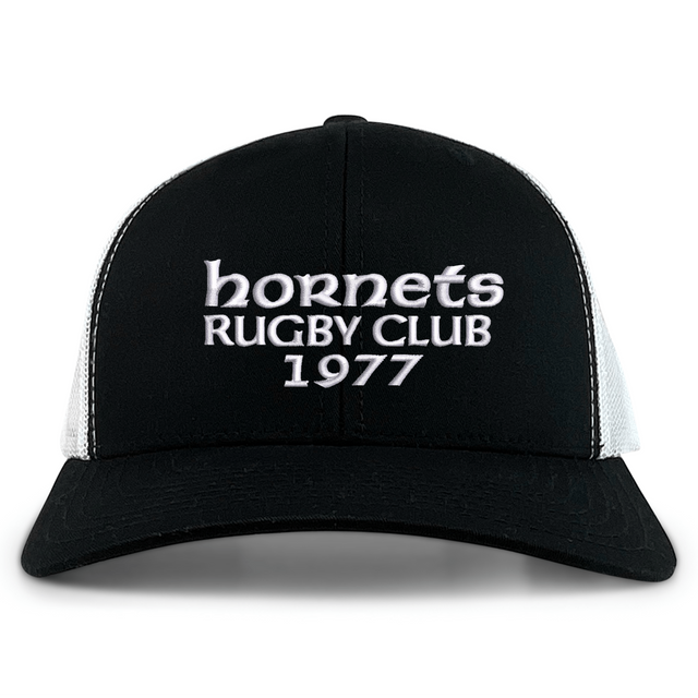 The Hornets Rugby Club 1977 Retro Trucker Cap by EMB S&S Activewear features an embroidered "hornets RUGBY CLUB 1977" design on the front, classic black and white color styling, and a comfortable snapback closure for an adjustable fit.