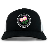 The Society of Iowa Rugby Referees Retro Trucker Cap by EMB S&S Activewear features a black and white design with a circular front logo adorned with pink flowers, embroidered on the front panel. The cap also includes an adjustable snapback closure for a comfortable fit.