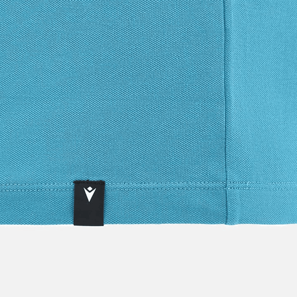 Close-up of a blue fabric with neat stitching and a small black tab featuring a white logo, embodying the elegance of the Italy 24/25 Travel Polo by Macron.