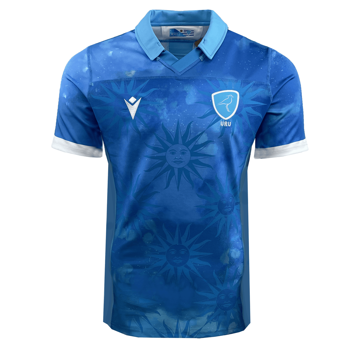 A Uruguay 24/25 Authentic Match Day Home Jersey by Macron, this blue short-sleeve soccer jersey boasts white accents, a patterned design of sun faces reminiscent of the Sol de Mayo, a bird crest with "URU," and the Macron logo.
