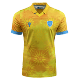 The Uruguay 24/25 Authentic Match Day Away Jersey by Macron is a yellow sports jersey with blue accents. It features a sun pattern and an emblem of a bird on the upper chest area, and is crafted from Eco-Armevo fabric for sustainable sportswear.