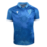 The Uruguay 24/25 Replica Home Jersey by Macron features a white collar, white sleeve cuffs, and sublimated sun designs with a face motif in striking blue and light blue hues. Crafted from Eco Fightex stretch fabric for optimal comfort and durability, the jersey also proudly displays a blue and white crest logo with "URU" text on the left chest.