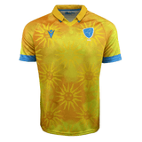The Uruguay 24/25 Replica Away Jersey by Macron is a yellow and orange rugby jersey, accented with blue trim and collar, featuring sun motifs, a blue crest with a bird and "URU" text, crafted from Eco Fightex stretch fabric.