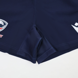 Close-up of USA Rugby 24/25 Home Shorts by Macron in navy blue, featuring visible stitching and two logo patches near the hem, designed for moisture-wicking performance.