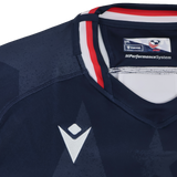 Close-up of the Women's USA Rugby 24/25 Home Bodyfit Shirt by Macron in navy blue, featuring white and red collar details, visible Macron logo, and "MPerformanceSystem" text on the collar tag.