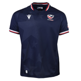 The USA Rugby 25/26 Replica Home Jersey by Macron features navy blue with subtle star patterns, red, white, and blue trim on the collar and sleeves, and the USA Rugby logo on the chest for authentic fan style.