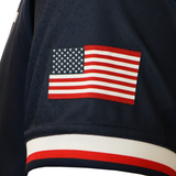 A close-up of a navy blue sleeve from the USA Rugby 25/26 Replica Home Jersey by Macron, showing an American flag patch and a red, white, and blue stripe near the cuff.