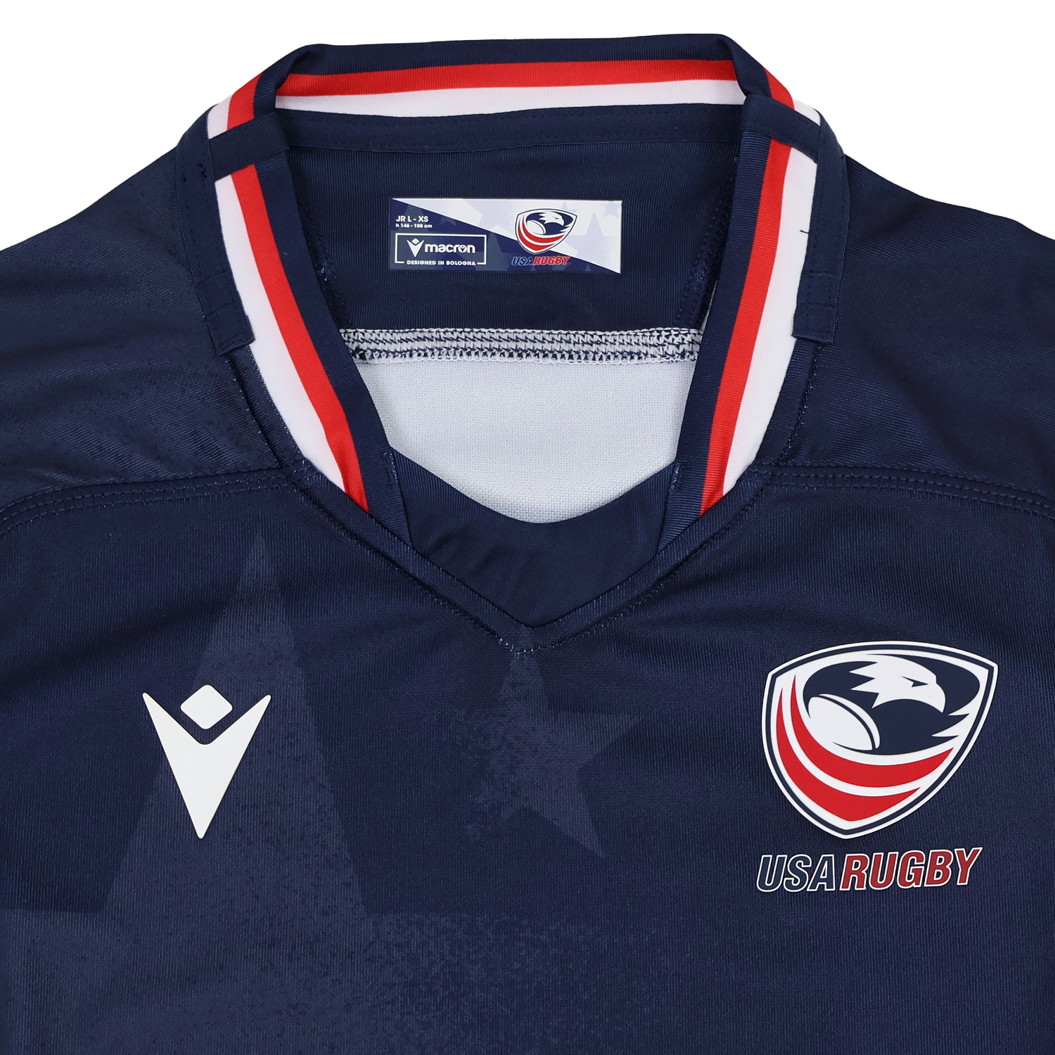 The Youth USA Rugby 24/25 Home Jersey by Macron is a navy blue jersey featuring the USA Rugby eagle logo, the Macron logo, and red, white, and blue collar accents.