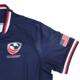 The Youth USA Rugby 24/25 Home Jersey by Macron features the team logo on the chest, an American flag patch on the sleeve, and red, white, and blue trim. A great choice for young fans to show USA Rugby pride.
