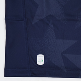 Close-up of navy blue fabric with subtle star patterns, visible stitching, and a small white "macron ECO" label near the hem—part of the Youth USA Rugby 24/25 Home Jersey by Macron.
