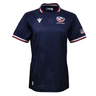 The Women's USA Rugby 25/26 Replica Home Jersey by Macron features a navy blue design, USA Rugby logo, white Macron logo, American flag patch on the sleeve, red-white-blue trim on collar and sleeves, and a subtle star pattern.