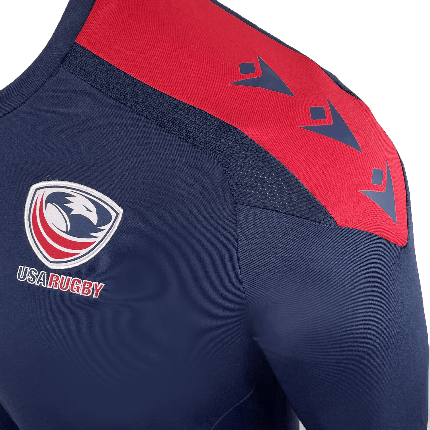 Close-up of the USA Rugby 25 Player Long Sleeve Training Shirt by Macron in navy blue and red, featuring the USA Rugby logo on the chest and three stylized blue arrow symbols on the shoulder.