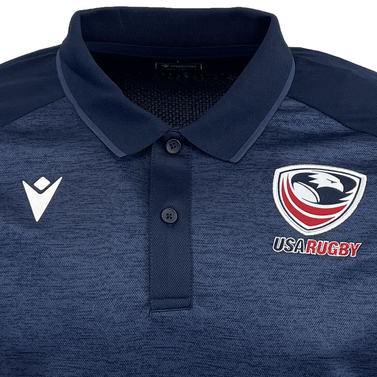 The USA Rugby 25 Travel Poly Polo by Macron is a navy blue polo featuring the USA Rugby eagle logo on the right chest and a white Macron logo on the left chest.