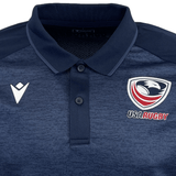 The USA Rugby 25 Travel Poly Polo by Macron is a navy blue polo featuring the USA Rugby eagle logo on the right chest and a white Macron logo on the left chest.