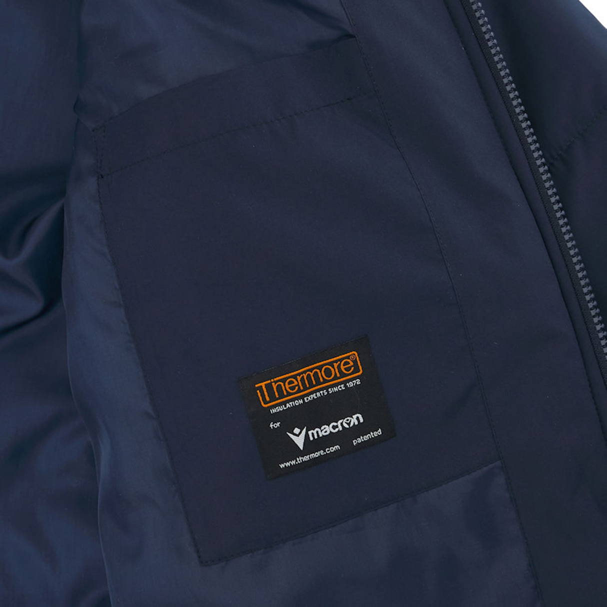 Close-up of the USA Rugby 25 Padded Bench Jacket by Macron in navy blue, featuring two internal pockets. One pocket shows a black label with orange and white text, indicating "Thermore" and "Macron," the official supplier for USA Rugby.