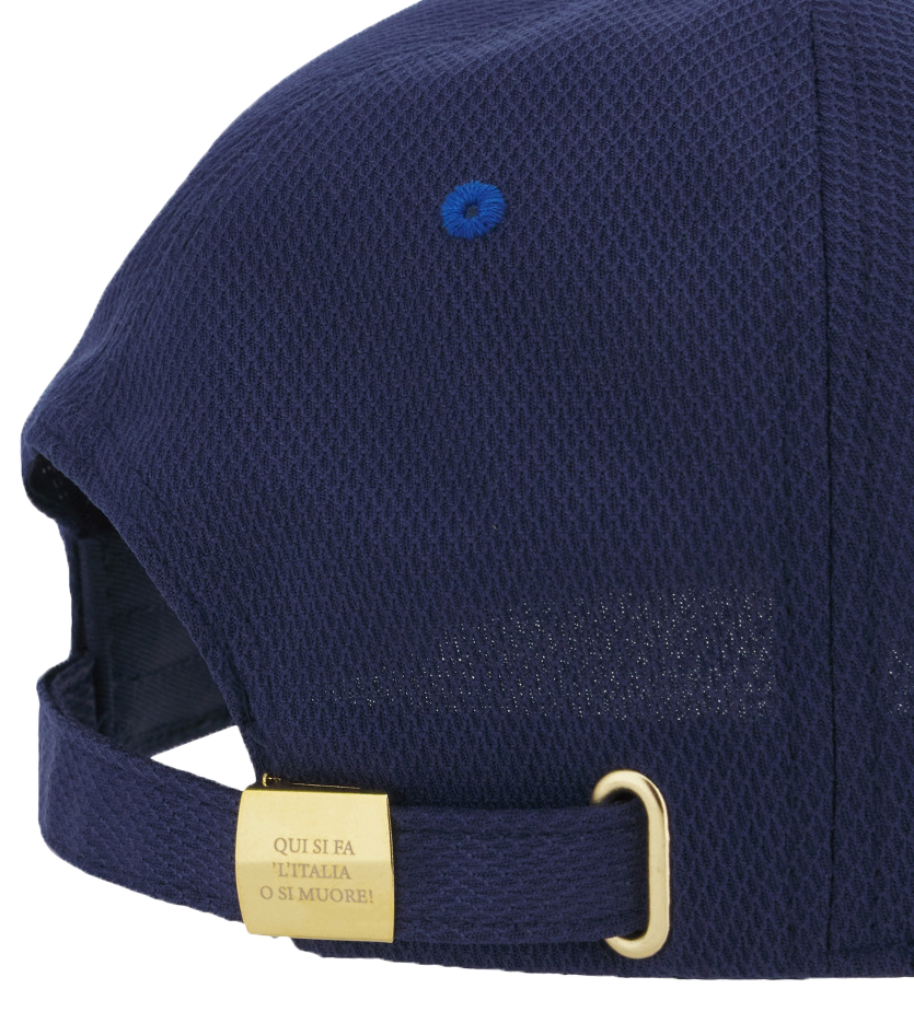 A close-up of the Italy 25/26 Supporters Cap by Macron in navy blue mesh, showing a gold buckle and a tag with "QUI SI FA L'ITALIA O SI MUORE!".