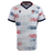 The USA Rugby 25/26 Home Body Fit Match Jersey by Macron features white fabric with red and blue star patterns, navy collar and sleeve trim, the USA Rugby logo on the chest, and an American flag patch on the sleeve for comfort and performance.