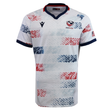 The USA Rugby 25/26 Home Body Fit Match Jersey by Macron features white fabric with red and blue star patterns, navy collar and sleeve trim, the USA Rugby logo on the chest, and an American flag patch on the sleeve for comfort and performance.