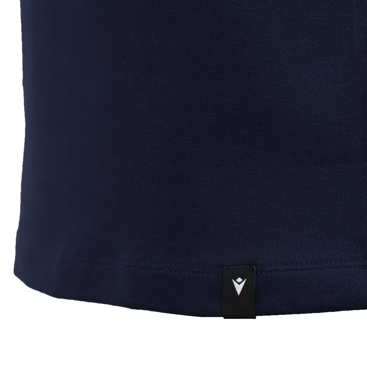 Close-up of the lower part of the USA Rugby 25/26 Athleisure Cotton Polo by Macron in navy blue, showing a small black tag with a white logo near the hem.