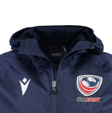 The USA Rugby 25/26 Rain Jacket by Macron is a navy blue waterproof zip-up with a hood, featuring the Macron logo on the left chest and the USA Rugby eagle logo with text on the right chest.