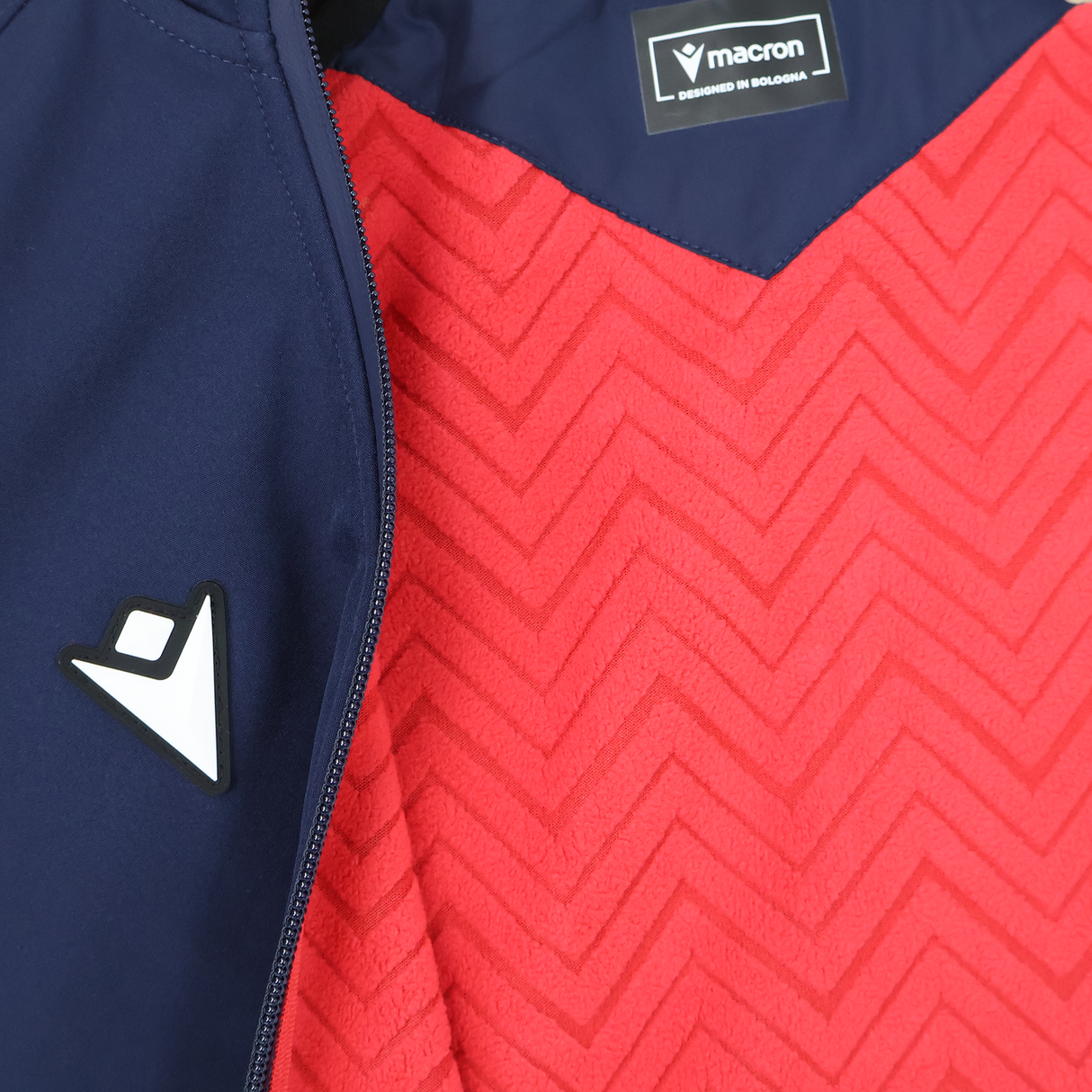 Close-up of the USA Rugby 25/26 Athleisure Softshell Jacket by Macron, navy blue and partially unzipped to show a red zigzag inner lining with visible logo—an ideal water-resistant jacket for athleisure style.