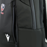 Close-up of the USA Rugby 25/26 Staff Backpack by Macron in black, showing a partially unzipped side pocket, rugby logo, and a white geometric emblem on the front.