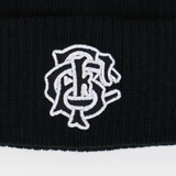 A close-up of the black Barbarians 25/26 Pom-Pom Beanie by Macron, featuring a white embroidered monogram logo with intertwined letters.