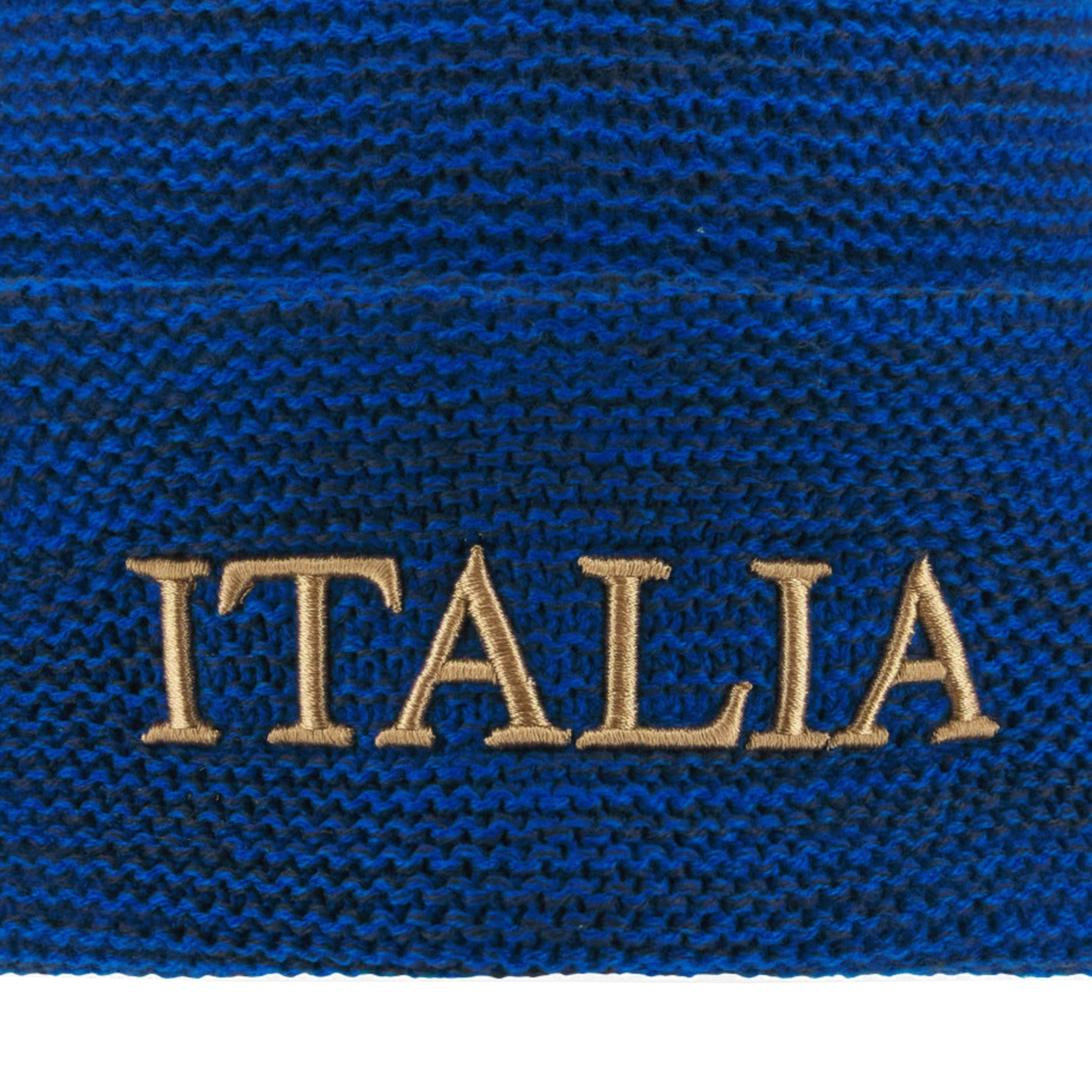 Close-up of blue knitted fabric from the Italy 25/26 Supporters Pom-Pom Beanie by Macron, showing "ITALIA" embroidered in beige thread.