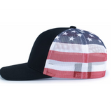 The Augusta Sportswear Printed Flag Trucker Cap features a black design with a mesh back and an American flag pattern in red, white, and blue with stars and stripes.
