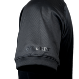 Close-up of the left sleeve of a black short-sleeved Gilbert Evo Performance Training Tee with "GILBERT" written in gray text above the hem.