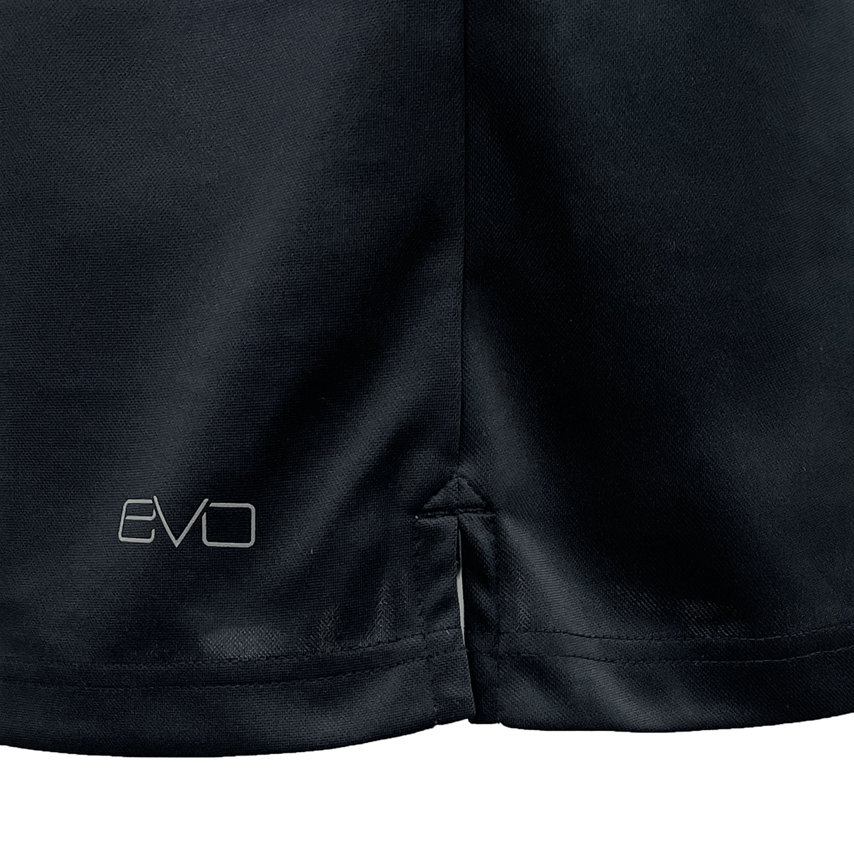 Close-up shot of the hem of a black Gilbert Evo Performance Training Tee by Gilbert, featuring a small slit and the word "EVO" printed in white.