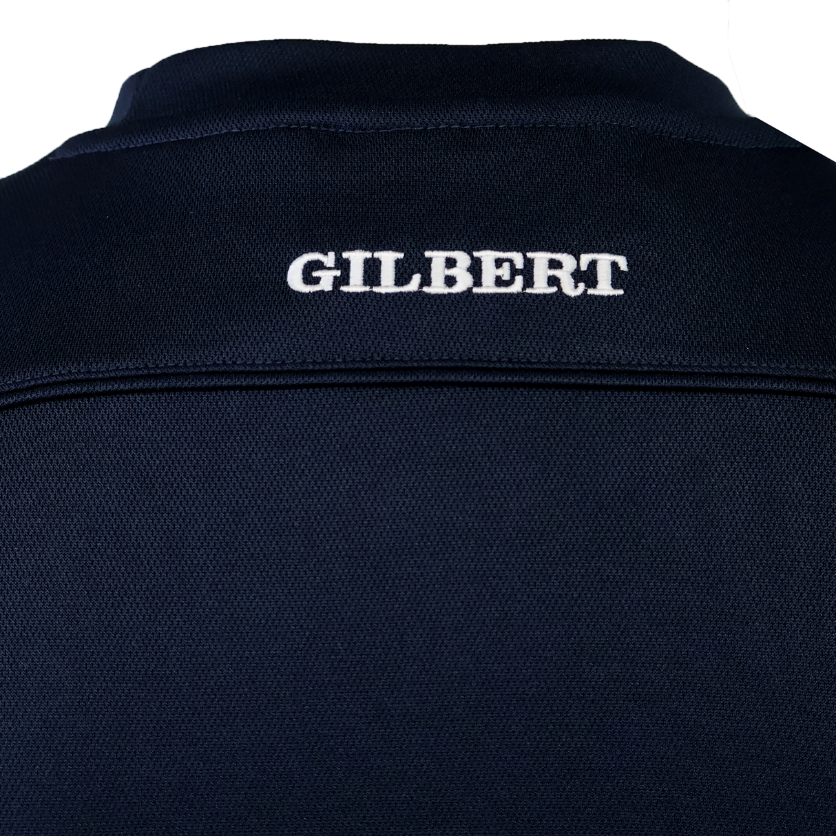 Close-up of the upper back of the Gilbert Photon Training Tee in dark navy, featuring "GILBERT" embroidered in white capitals. This moisture-wicking tee by Gilbert offers added comfort during training.