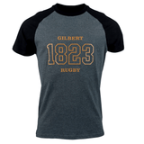 A dark gray and black raglan Gilbert Rugby 200 Year Anniversary Leisure Shirt by Gilbert features the text "Gilbert Rugby 1823" in bold gold letters on the front, celebrating its rich rugby history.