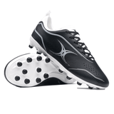 A pair of Gilbert Cage Torq MSX FG - Black/White soccer cleats is displayed, with one shoe upright and the other laid on its side showcasing a multi-surface sole ideal for various pitches.