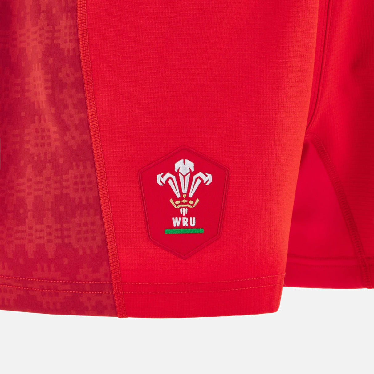 Close-up of Wales 25/26 Matchday Home Shorts by Macron, showcasing the WRU logo with three white feathers and a green banner on the lower leg.