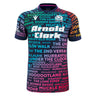The Scotland 25/26 Rainbow Training Jersey by Macron features short sleeves and showcases colorful Scottish-themed words and phrases in various fonts on a dark background.